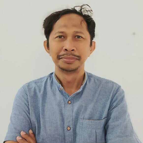 Croppedcroppedwhatsappimage20221213at10 55 58 catrawarta Man with short black hair and goatee wearing a light blue button up shirt standing against a white background